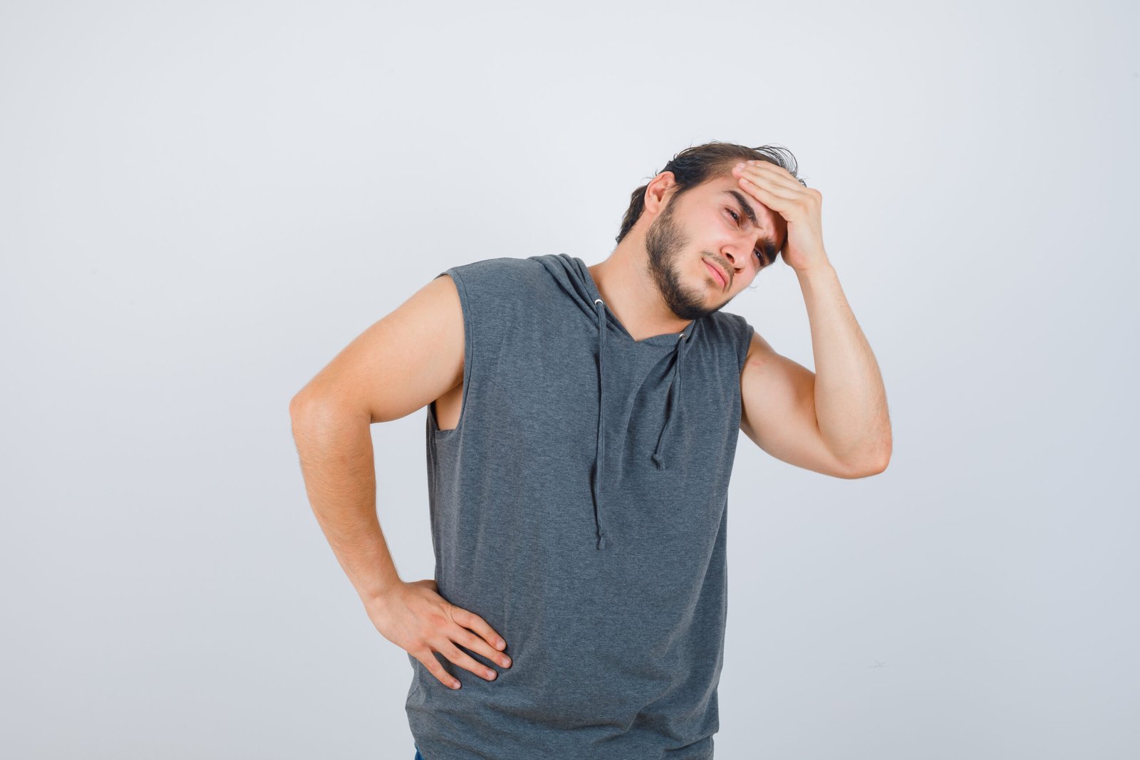 young fit male keeping hand on forehead in sleeveless hoodie  and looking painful , front view